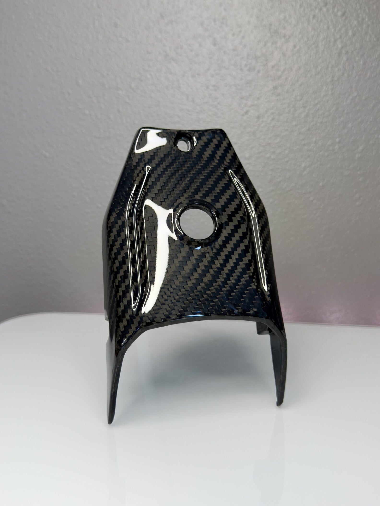 Carbon fiber part on a white surface with a gray background